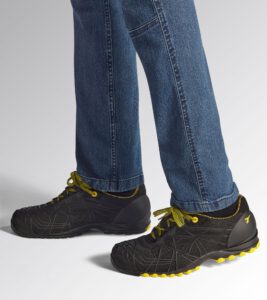 Primer plano lateral de zapatillas de seguridad Diadora Beat negras y amarillas puestas con vaqueros azules. Muestra el diseño ligero y deportivo en un entorno laboral de Zaragoza. Calzado de seguridad cómodo disponible en Cuarte de Huerva.